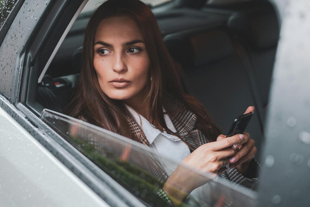 A Karen looking out of a car window while holding a smartphone, portraying a modern lifestyle.